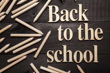 Letters Forming the Words ''Back to School'' with a few color pencils on dark wooden background