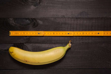 Old and dirty folding carpenter's ruler next to banana on dark wooden backgroundの写真素材