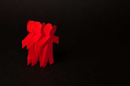 Group of paper doll holding hands. Teamwork concept papercraft. Orange dolls on black wooden backgroundの写真素材