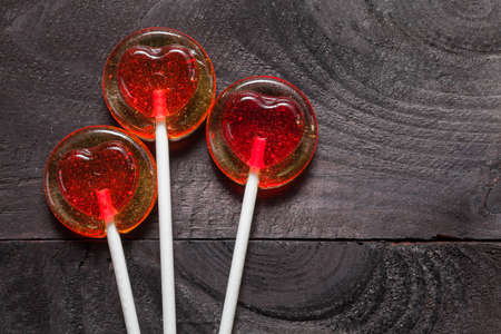Red heart shaped candy lollipop on black wooden backgroundの写真素材