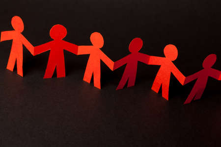 Group of paper doll holding hands. Teamwork concept papercraft. Orange dolls on black wooden backgroundの写真素材