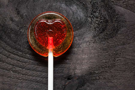 Red heart shaped candy lollipop on black wooden backgroundの写真素材