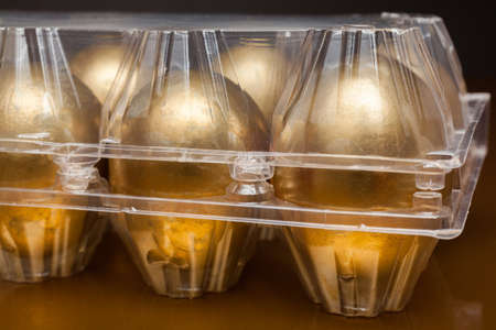 Golden eggs in a plastic box on golden backgroundの写真素材