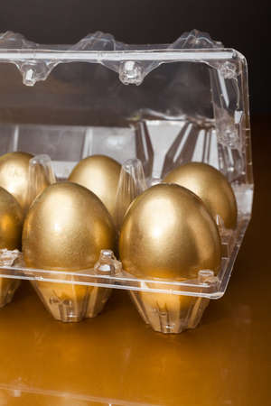 Golden eggs in a plastic box on golden backgroundの写真素材