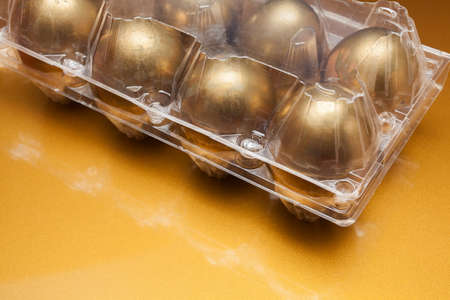 Golden eggs in a plastic box on golden backgroundの写真素材