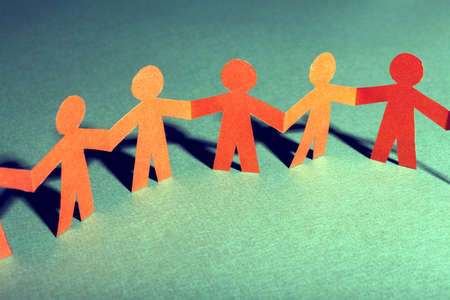 Group of paper doll holding hands. Teamwork concept paper craft. Orange dolls on green background

