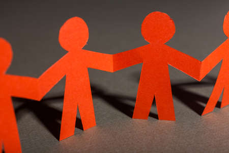 Group of paper doll holding hands. Teamwork concept paper craft. Orange dolls on gray background

の写真素材