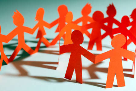 Group of paper doll holding hands. Teamwork concept paper craft. Orange dolls on black wooden background

の写真素材