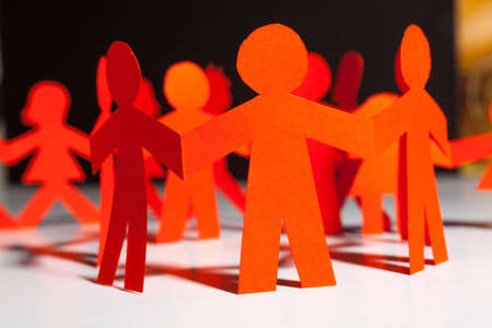 Group of paper doll holding hands. Teamwork concept paper craft. Orange dolls on black wooden...