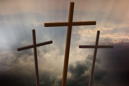 Three wooden crosses stand against a dramatic evening sky with radiant beams penetrating clouds