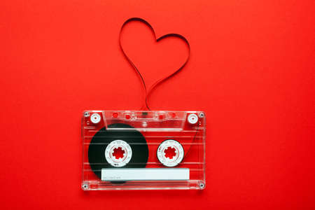 Vintage audio cassette with loose tape shaping a heart on red background の写真素材