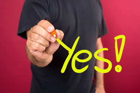 Young casual man writing the word YES on glass board with marker の写真素材