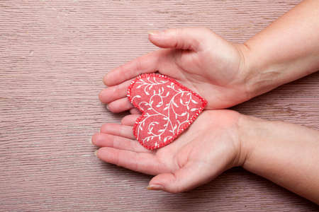 Female's hand holding a fabric heart against woodgrain textured wall の写真素材