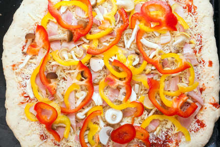 Preparing a pizza putting various ingredients over the dough before cooking.の写真素材