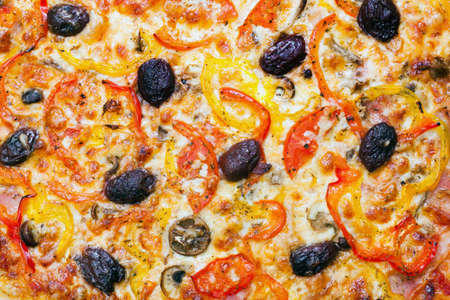 Close up photo of the surface of homemade pizza with mushrooms, tomato, peppers, olives and melted cheese の写真素材