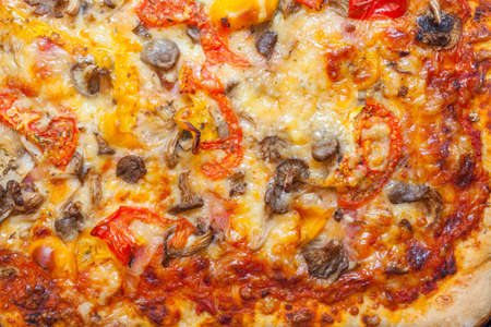 Close up photo of the surface of homemade pizza with mushrooms, tomato, peppers, olives and melted cheese の写真素材