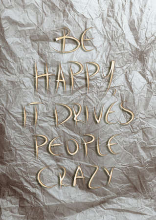 BE HAPPY, IT DRIVES PEOPLE CRAZY quote on a crumpled piece of paper background の写真素材