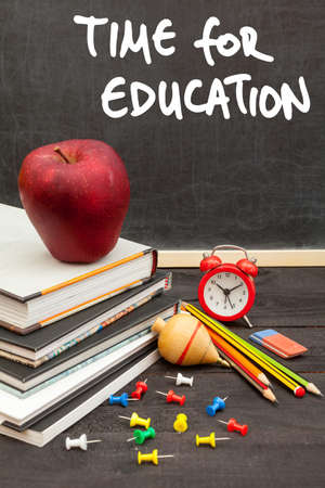 Apple on books and time for education handwritten on the chalkboard in the background