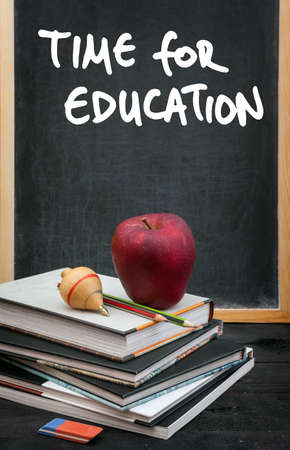 Apple on books and time for education handwritten on the chalkboard in the background