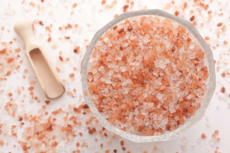 Himalayan salt in glass bowl next a wooden scoop on white backgroundの写真素材