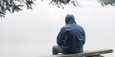 Depressed man sitting on bench in hooded jacket