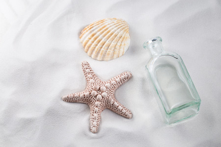 A starfish, a sea shell and an empty bottle on white exotic clean sand.の写真素材