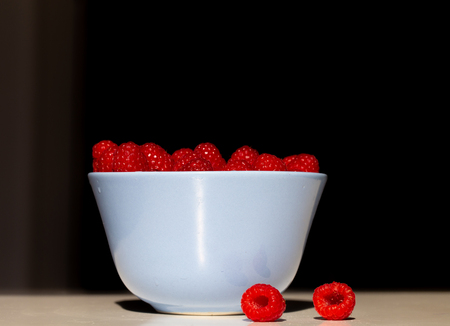 Delicious fresh fruity raspberries in a blue bowl on black backgroundの写真素材