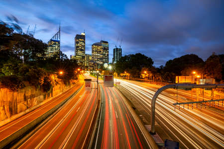 Sydney City Skyline at sunset with car light trails from the Eastern Distributor Motorway in the...