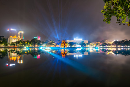 Spectacular night light show illuminating Turtle Tower at Hoan Kiem Lake with colorful beams...