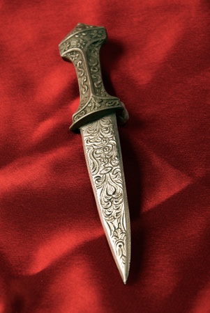 Antique dagger with detailed patterns on red stain background
