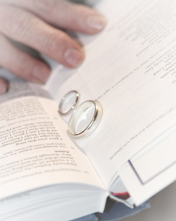 Two wedding rings in the center of an open bible with a portion of a hand showingの写真素材