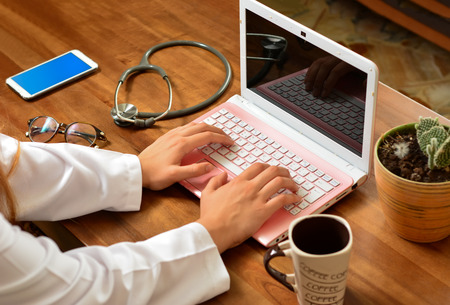 Doctor working on laptop computer and medical stethoscope on clipboard on deskの写真素材