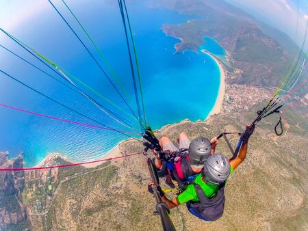 Mugla, Fethiye, Turkey June 15, 2019: Extreme sport. Landscape. Paragliding in the sky. Paraglider tandem flying over the sea in the mountains. Aerial view of paraglider and Blue Lagoon in Oludeniz, Turkey.の写真素材