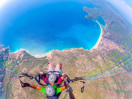 Mugla, Fethiye, Turkey June 15, 2019: Extreme sport. Landscape. Paragliding in the sky. Paraglider tandem flying over the sea in the mountains. Aerial view of paraglider and Blue Lagoon in Oludeniz, Turkey.の写真素材