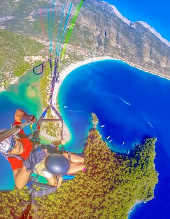 Extreme sport. Landscape. Paragliding in the sky. Paraglider tandem flying over the sea in the mountains. Aerial view of paraglider and Blue Lagoon in Oludeniz, Turkey.の写真素材