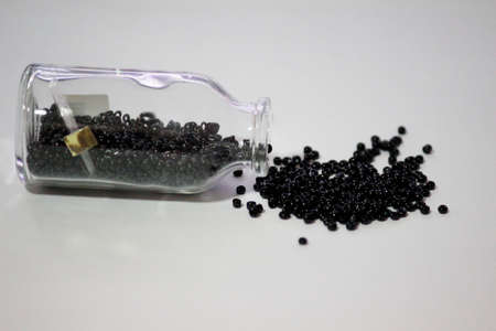 Black beads pour out from a glass design bottle with background