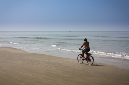 a man riding a bicycle along the ocean beachの写真素材