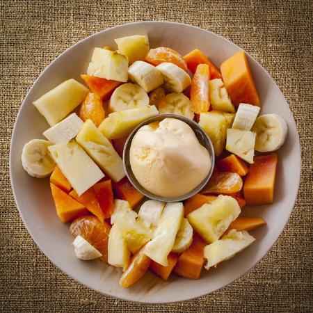 tropical fruit salad with ice cream in a plate served on rustic burlap fabricの写真素材