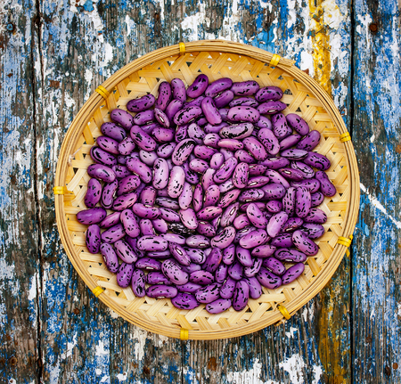 spotted purple beans in a woven bamboo bowl on a rustic wooden backgroundの写真素材