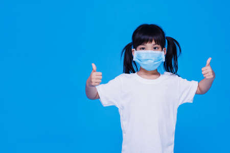 Asian little cute girl wearing a  mask to protective spread the disease on Blue background. Prevention of spreading the corona virus COVID-19 cold flu or pollution.の写真素材