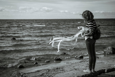 A black and white photo of a girl with ribbons standing with her back to the waterの写真素材