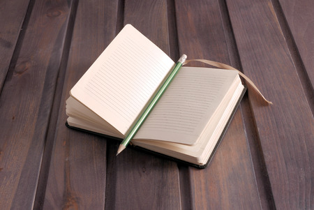 Open blank notebook on dark wood background in green color with green pencil