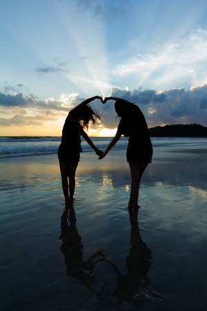 Romantic young couple making heart shape with arms on beach at sunset  beautiful sky.の写真素材