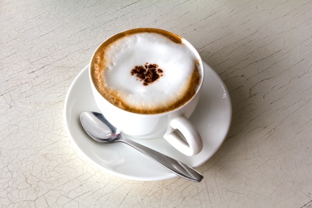 Coffee cup with artistic cream decoration, isolated on old white wood backgroundの写真素材