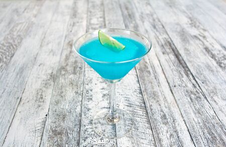 Frozen Blue Margarita Cocktail in martini glass with lemon isolated on wood tableの写真素材