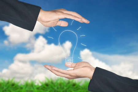 2 hands protects light bulb icon, against skyscapeの写真素材