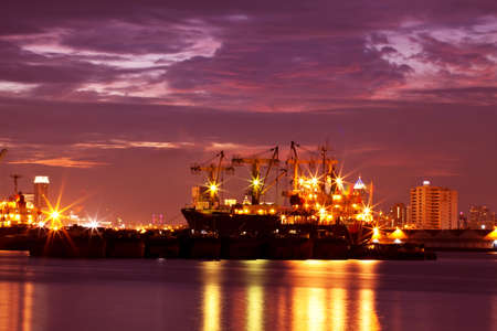 Image of the illuminated cargo port in Thailand at sunset with container terminals, cargo ships and cranes at sunset backgroundの写真素材
