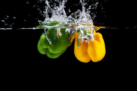 Yellow and green sweet pepper splash into a black color of waterの写真素材