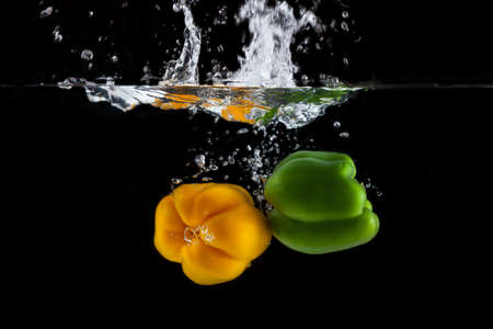 Yellow and green sweet pepper splash into a black color of waterの写真素材