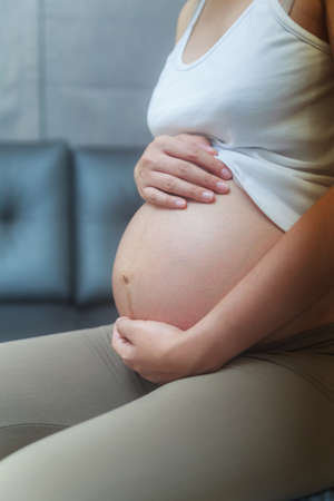 Pregnant woman putting hand on the belly while sitting on sofaの写真素材